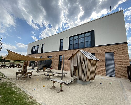 Kita-Gebäude von der Rückseite mit Sand-Spielplatz